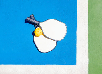 Two pickleball paddles and a yellow ball rest on a blue and green outdoor court.