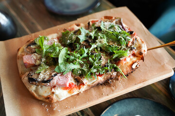 Traditional Italian pizza with arugula and tomatoes on a dark background.