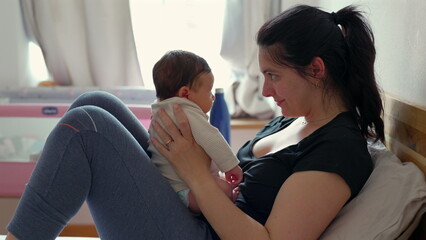 Mother and baby share a tender moment on the bed, with their foreheads touching, creating a bond of love and connection in a cozy and intimate setting