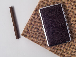 Mini cigar with storage case made of leather, lying on burlap fabric on white background