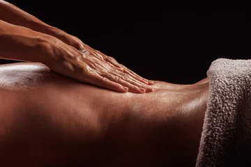 Girl gives back massage to muscular man on dark background close-up, beautiful relaxing male massage © st.kolesnikov