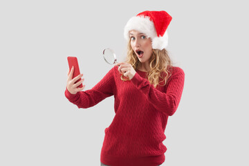 Amazed Santa Claus woman looks at her smartphone, searching for Christmas presents, while holding a...