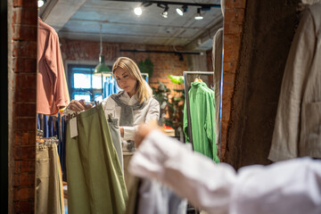 Fashionable woman picks clothes, checks price tags before trying outfits in shopping mall. Female...
