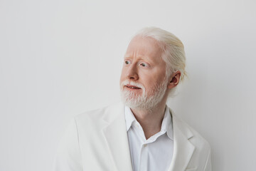 Obraz premium Elderly man with white hair and beard, dressed in a white suit, looking thoughtfully to the side against a minimalistic white background, exuding wisdom and elegance