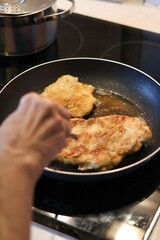 Close-up of an elderly woman's hand frying cutlets in a pan