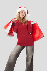 Happy merry Christmas woman wearing Santa hat holds red shopping bags and blow a kiss to camera. For sale offer promotions, online shopping, advertise banner, poster or gift card, isolated background