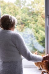 A lonely elderly woman standing at the window and waiting