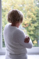 A lonely elderly woman standing at the window and waiting