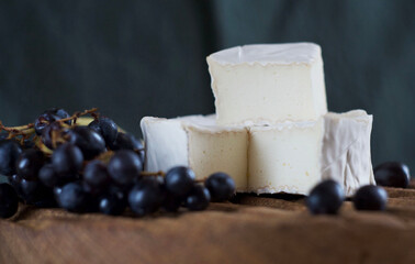 Camembert cheese lies on a wooden board, grapes lie nearby