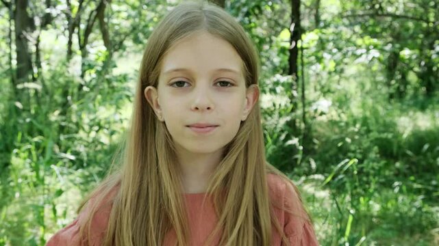 The girl in the forest smiles and tucks her hair behind her ear.