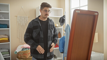 Handsome hispanic man adjusting shirt in a well-organized, modern dressing room with mirror and shelving.