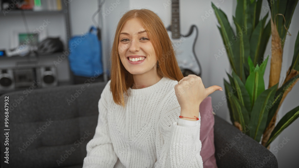 Canvas Prints Smiling young redhead woman pointing with thumb indoors at a cozy apartment