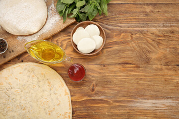 Raw dough, crust and ingredients for preparing pizza on wooden background