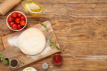 Board with raw dough and ingredients for preparing pizza on wooden background