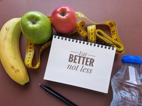 Eat better not less, motivation quote written on notebook. Healthy nutrition inspirational message with apples, banana, water and measuring tape. Motivational phrase, sport and healthy eating concept.