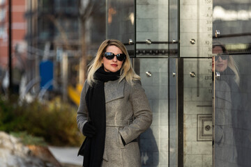 Close-up portrait of a young blonde Caucasian woman with long hair in a jacket in the city outdoors on a sunny day against the background of the parking lot. Model posing with a smile.