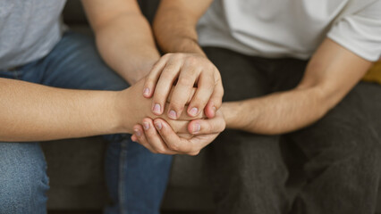Fototapeta premium Two men holding hands in a supportive gesture, symbolizing friendship or comfort in a casual indoor setting.