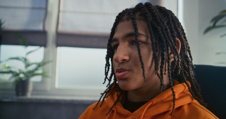 Portrait of depressed African American teenage boy discussing family problems or psychological trauma with psychologist on counseling session. Upset teenager during therapy with psychotherapist.