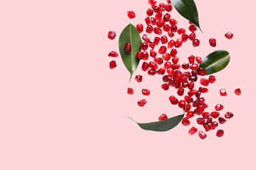 Flying fresh pomegranate seeds and leaves on pink background