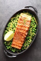 Delicious grilled salmon fillet with green peas and lime in baking dish on grey textured table, top view