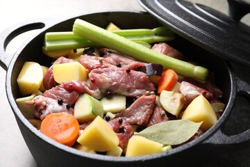 Cooking stew. Uncooked meat and vegetables in pot on light grey table, closeup