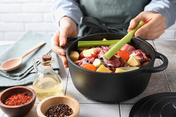 Woman preparing stew with vegetables and meat at white tiled table, closeup