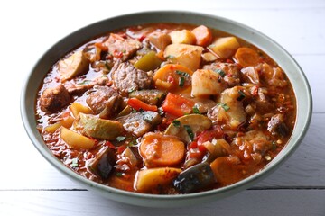 Delicious stew with vegetables in bowl on white wooden table, closeup