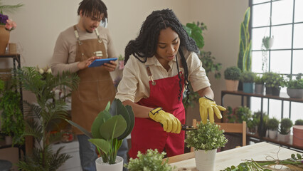 A woman and man work together in a well-stocked, sunlit flower shop, arranging plants and handling...