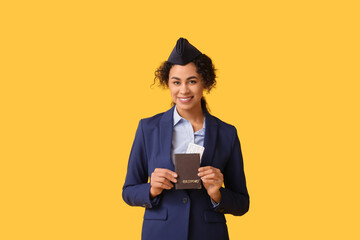 Beautiful African-American stewardess with passport and ticket on yellow background