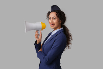 Beautiful young African-American stewardess with megaphone on grey background