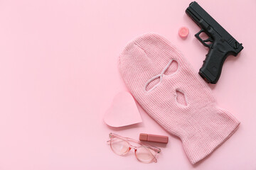 Composition with balaclava, gun and female accessories on pink background