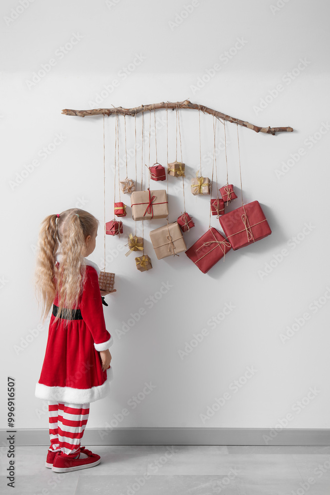 Wall mural cute little girl in santa costume with christmas advent calendar hanging on light wall