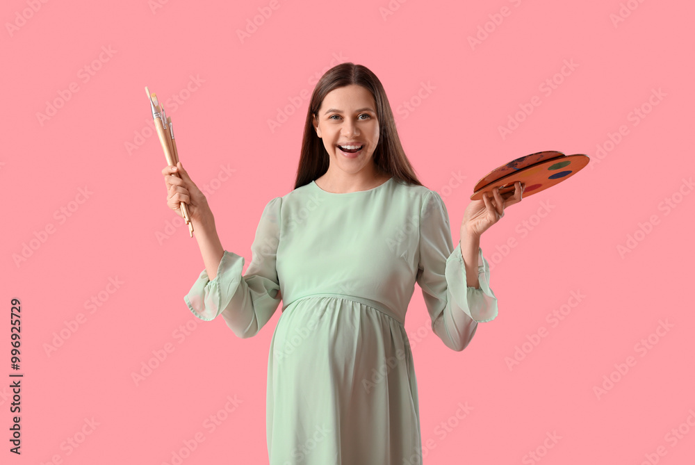 Poster Young pregnant female artist with brushes and palette on pink background