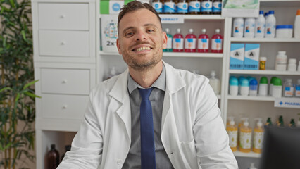 Smiling pharmacist man in white coat at pharmacy with shelves of medication