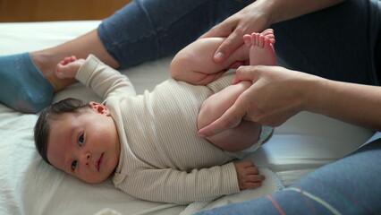 Mother holding baby's feet and gently bicycling his legs to help him relieve gas. Bright and...