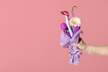 Woman holding bouquet with flowers and vibrators on pink background