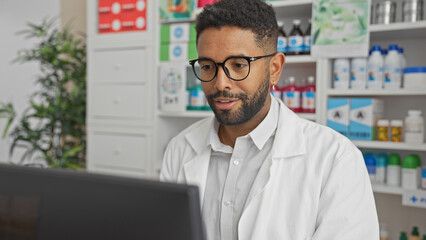 A young adult black man with glasses and a beard working on a computer at a pharmacy store