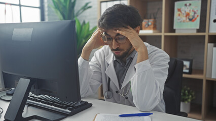 Stressed young man with beard in white lab coat at clinic office