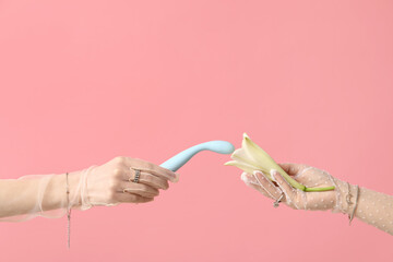 Female hands in laced gloves with vibrator and lily flower on pink background