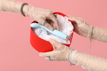 Women in lacing gloves putting vibrator into gift box against pink background, closeup