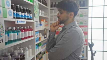 Fototapeta premium A thoughtful man with a beard considering options in a modern pharmacy full of medical products.