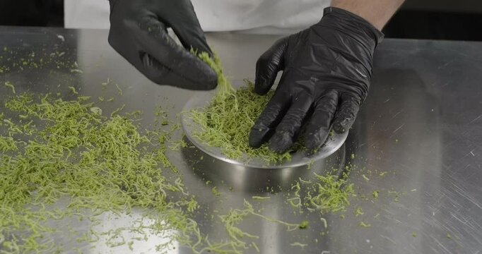 Pastry chef tamp kataifi dough with pistachios in the copper plate with hands. Traditional Turkish dessert kunefe or kunafa. Close-up