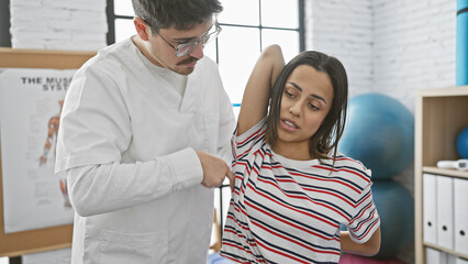 Obraz premium A female patient receives shoulder examination from a male therapist in a physiotherapy clinic.