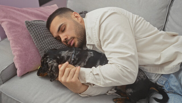 A handsome, young, hispanic man sleeping on a couch in a cozy living room, hugging his teckel dog, showcasing the warmth and comfort of home and companionship.