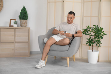 Obraz premium Sporty young man with pulse oximeter sitting in armchair at home