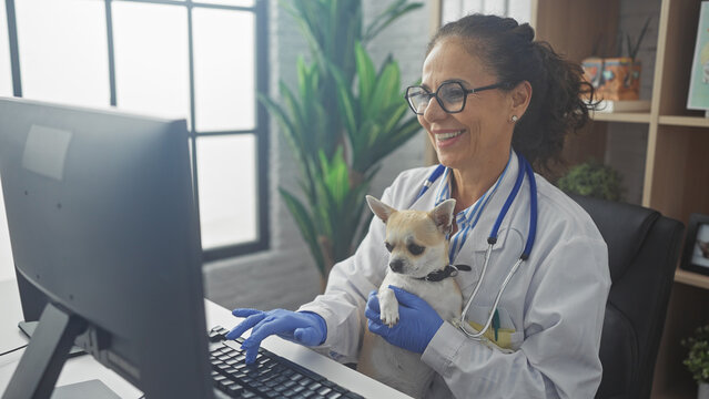A smiling hispanic woman veterinarian holding a chihuahua dog inside a veterinary clinic.