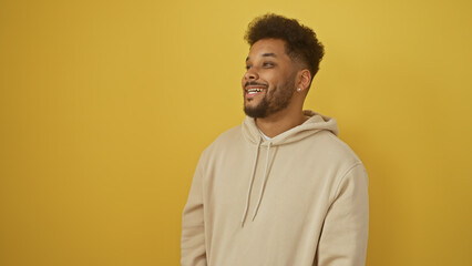 Handsome african american man smiling in casual beige hoodie against a vibrant yellow background.