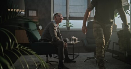 Military man shakes hands with senior psychologist and leaves after successful rehabilitation or psychological therapy. Satisfied therapist says goodbye to soldier and smiles while sitting in chair.