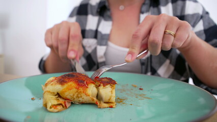 Person in checkered shirt cutting into a serving of homemade enchiladas on a green plate, ready to enjoy a tasty meal