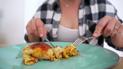 Person in checkered shirt cutting into a serving of homemade enchiladas on a green plate, ready to enjoy a tasty meal
